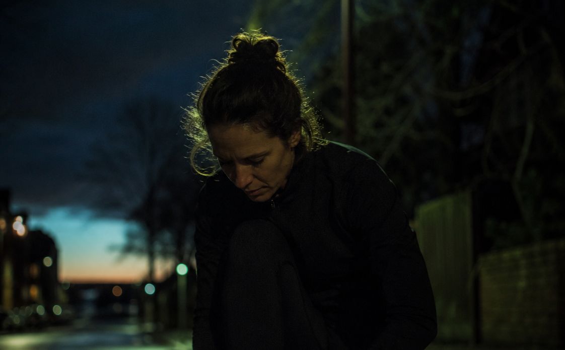 A runner tying her shoes under a streetlamp before a dawn run